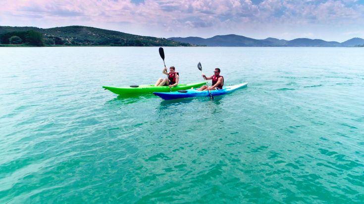 Two people kayaking on Lake Trasimeno, surrounded by serene nature and hills.