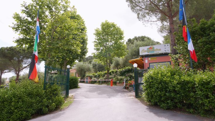 Entrance of Camping Village Cerquestra, surrounded by trees and lush greenery, showcasing a tranquil scene.
