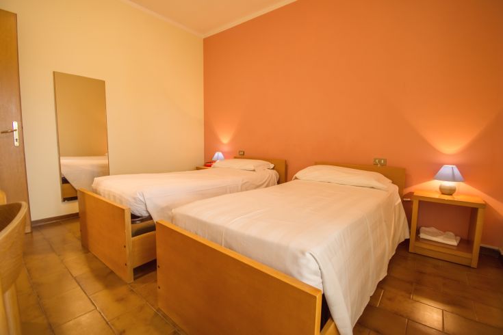 Camera accogliente con letti singoli e tonalità calde, dispone di arredamento essenziale.