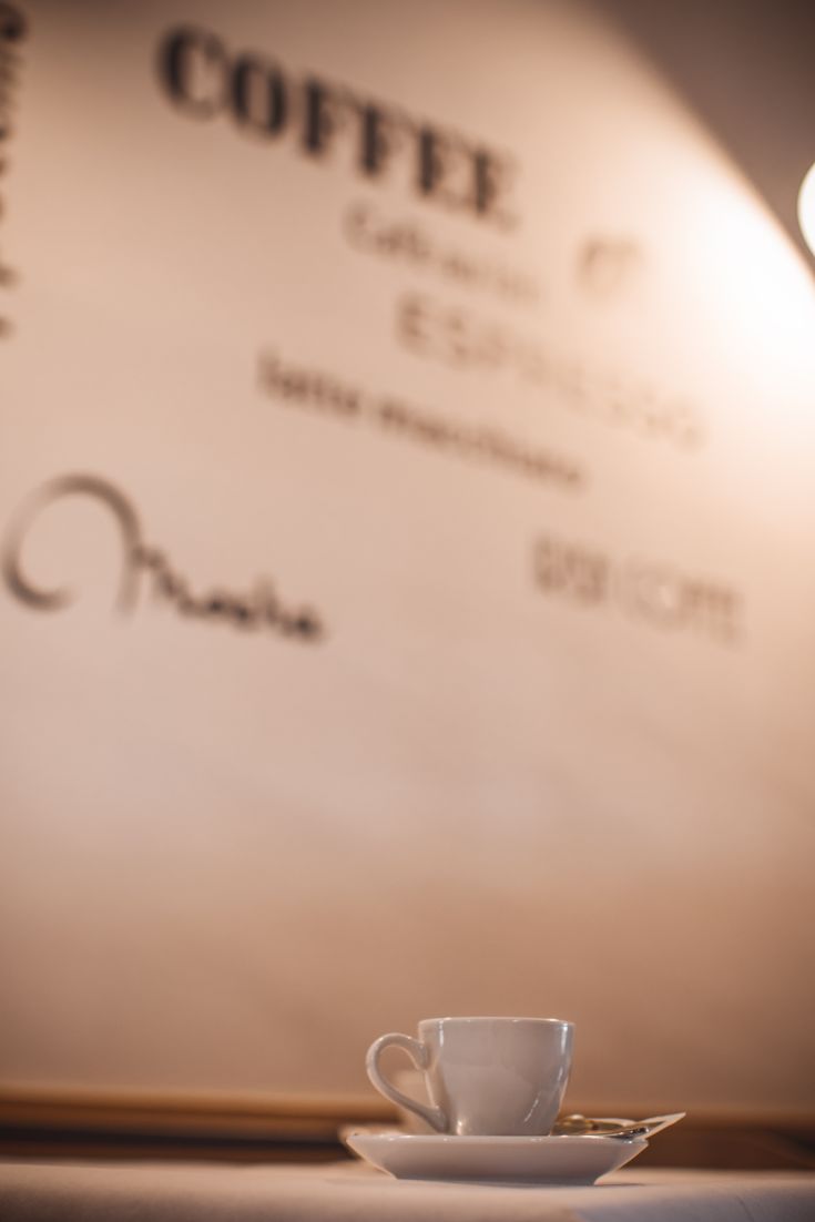 Una tazza di caffè su un tavolo in un ambiente rilassato con un muro decorato da scritte. Atmosfera semplice e confortevole.