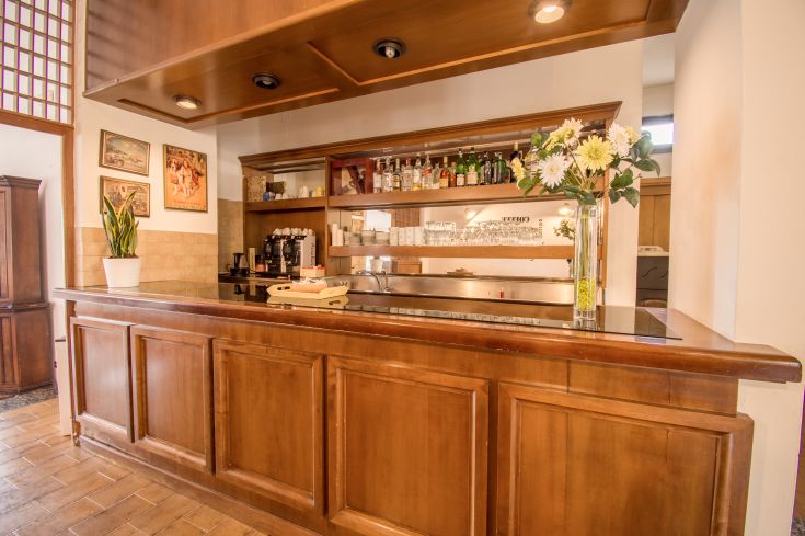 Interno di un palazzo con un bancone bar in legno e fiori freschi ben disposti.