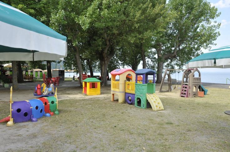 Un espace de jeux pour enfants, entouré d'arbres et de plantes, situé près d'un lac.