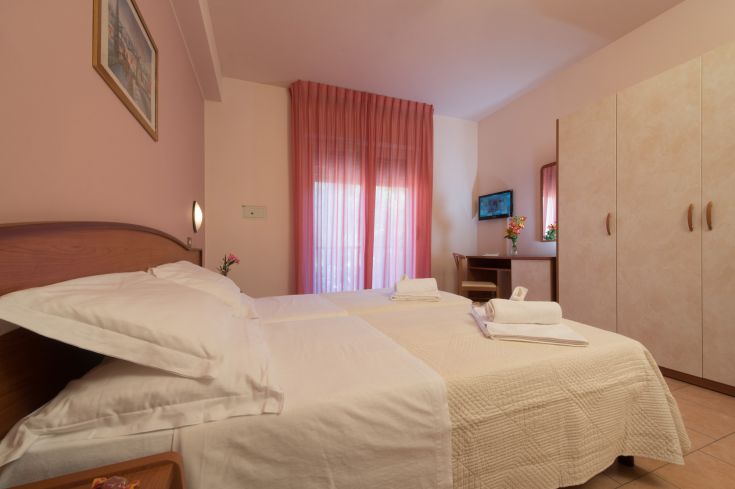 Chambre de l'Hôtel Torricella, décor simple avec des lits confortablement disposés et des détails décoratifs dans des tons roses.