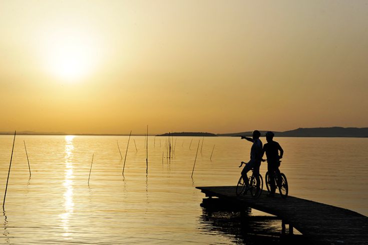 Deux cyclistes regardent le coucher de soleil sur le lac Trasimeno depuis le sommet d'un débarcadère.