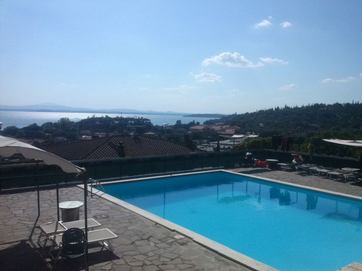 Une vue panoramique montrant la piscine et le lac Trasimeno, avec un hôtel entouré d'espaces verts.