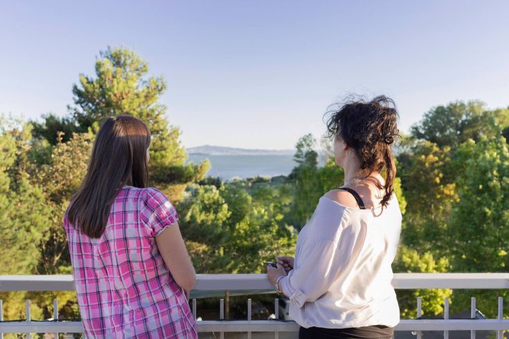 Two women observe the lake, surrounded by lush vegetation.
