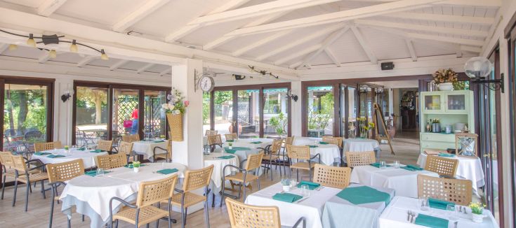 Renovated restaurant veranda with simple furnishings, overlooking a green area with neatly arranged tables.