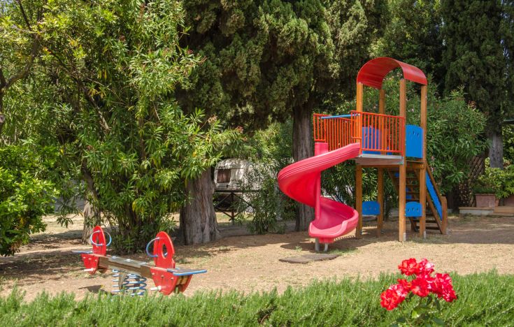 A playground surrounded by trees and grass, featuring a red slide and a swing, perfect for entertaining children.