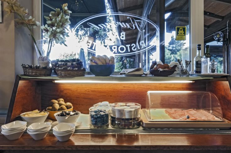 A breakfast buffet is set up in a cozy veranda overlooking a lake.