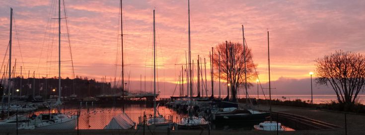 Panorama di un porto al tramonto, con imbarcazioni e un cielo dai toni caldi.
