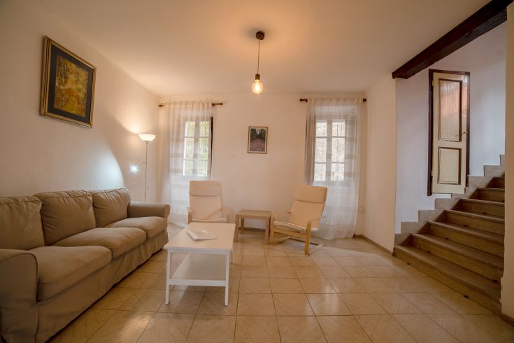 Un soggiorno semplice con un divano e alcune sedie, illuminato da luce naturale. L'ambiente è caldo e invitante.