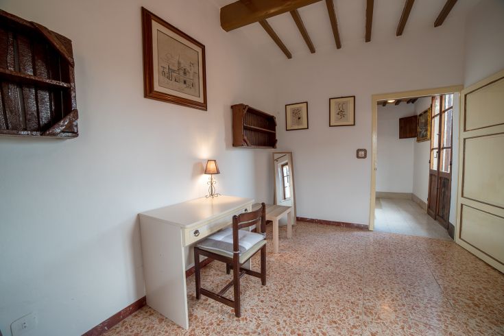 Una stanza ben illuminata con mobili essenziali, inclusi uno scrittoio in legno e una lampada da tavolo.