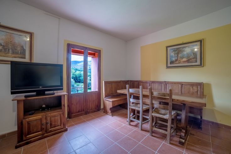 Interno di un palazzo con un tavolo in legno e uno spazio caratterizzato da una scenografia naturale fuori dalla finestra.