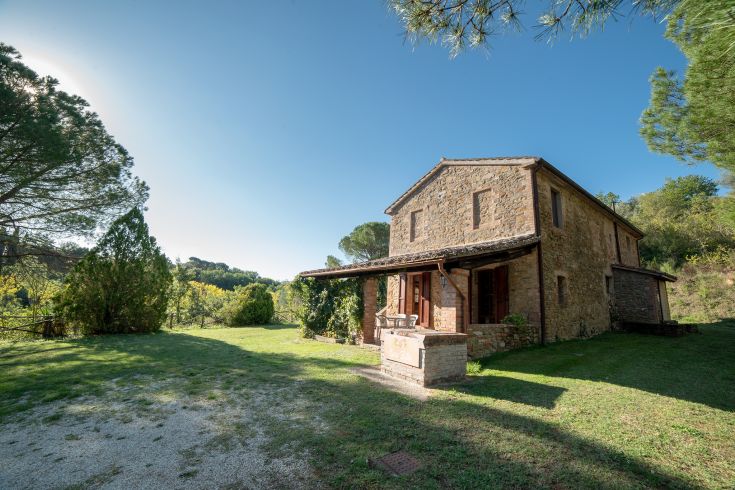 Una casa colonica circondata da un ampio spazio verde, con alberi e vegetazione che la circondano.