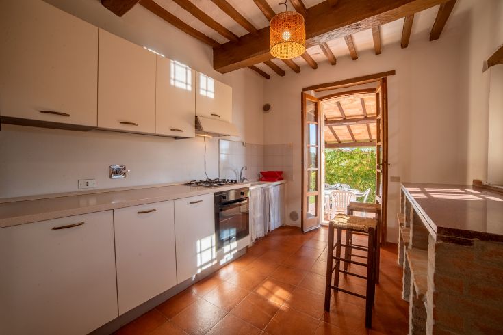 Cucina ben illuminata con elementi rustici e accesso diretto a uno spazioso patio esterno.