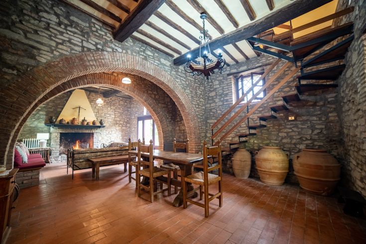 Ambiente rustico con pareti in pietra, un tavolo in legno e una scala comoda in legno.