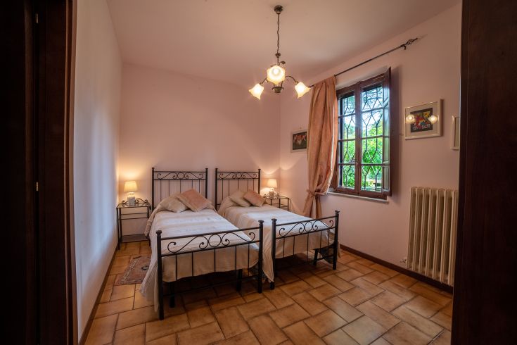 Camera semplice in agriturismo, con letti singoli e luce tenue, affacciata su un giardino.