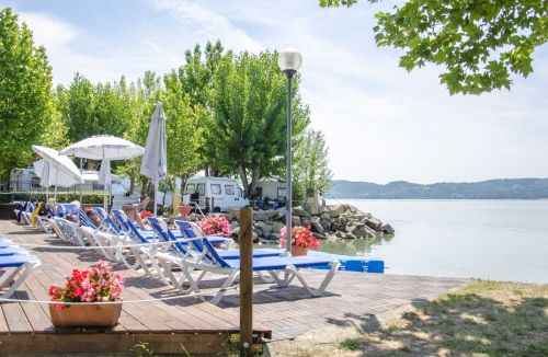 A relaxing area with sunbeds and umbrellas by the lake, surrounded by greenery and tranquility.