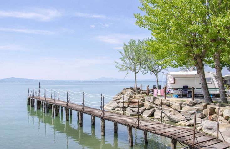 A serene scene featuring a pier by a lake, surrounded by trees and a camping area.