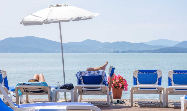 Relaxing moments by Lake Trasimeno with sun loungers and umbrellas, surrounded by nature.