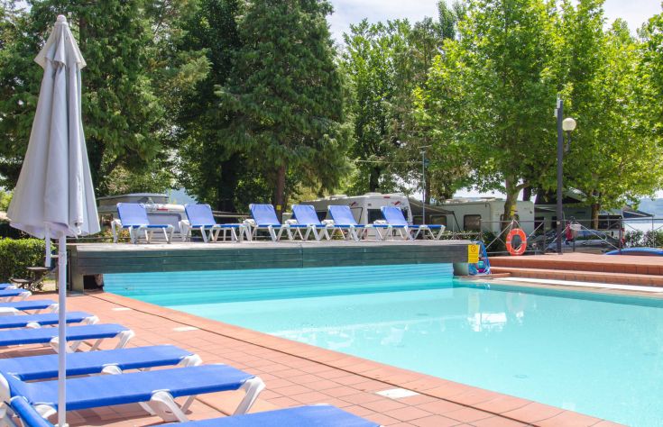 Swimming pool in a green area, equipped with sunbeds and umbrellas for relaxation.