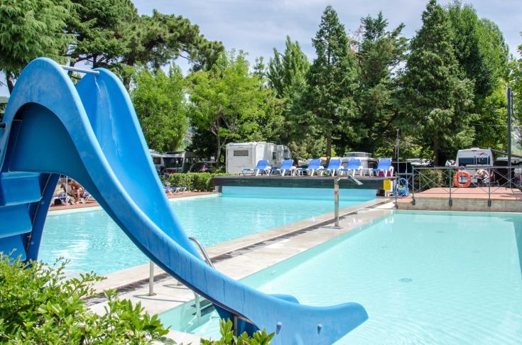 Camping area featuring a pool with slides, surrounded by trees and lush vegetation.