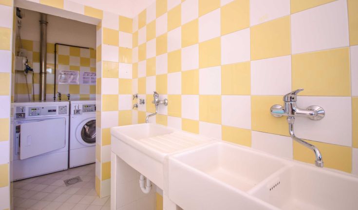Laundry room with yellow and white tiles, featuring sinks and washing machines.