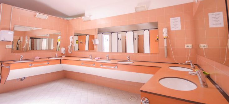 A spacious bathroom with pink walls, featuring multiple sinks and toilets.