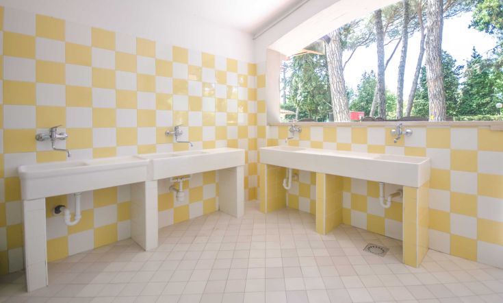 Camping Kursaal bathroom, decorated with yellow and white tiles, surrounded by lush greenery.