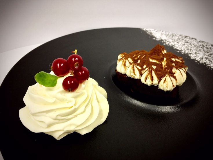 Delikates Dessert mit Schlagsahne und roten Früchten, serviert auf einem schlichten Teller.