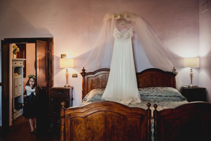 A room with a wedding dress hanging, as a curious girl enters.