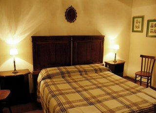 Camera semplice con letto matrimoniale, illuminata da lampade soffuse. Ambiente tranquillo e confortevole.