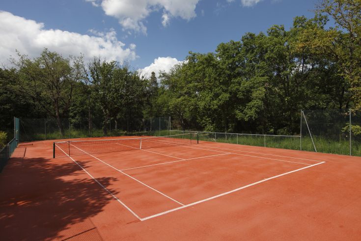 Campo da tennis situato all'aperto, circondato da vegetazione e sotto un cielo limpido.
