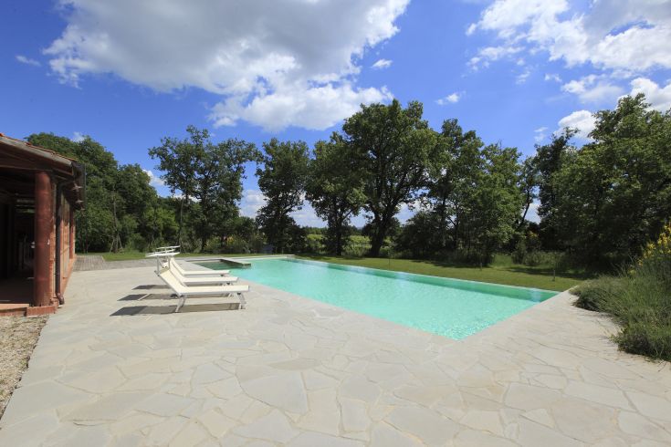 Una piscina tranquilla immersa nel verde, circondata da alberi e sotto un cielo sereno.