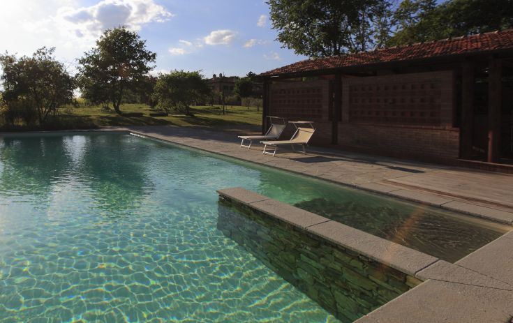 Una piscina tranquilla circondata da un giardino curato, con un palazzo elegante che si erge sullo sfondo.