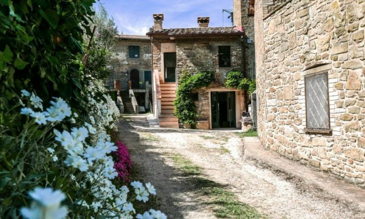 Agriturismo circondato da un contesto naturale, con strutture storiche e piante lungo il percorso d'accesso.