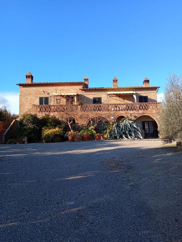 Una semplice casa di campagna immersa nel verde, circondata da un giardino e sotto un cielo chiaro.