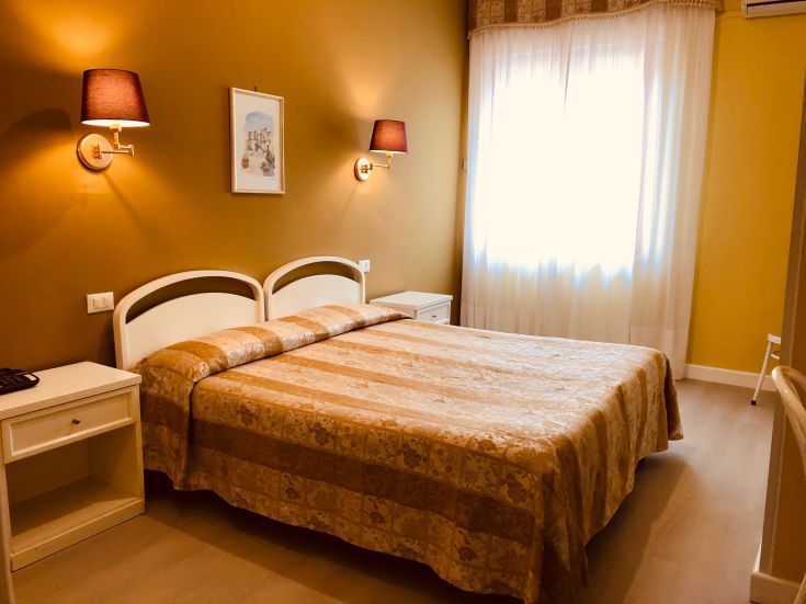 Chambre avec lits simples, éclairage chaud et grande fenêtre offrant une lumière naturelle.