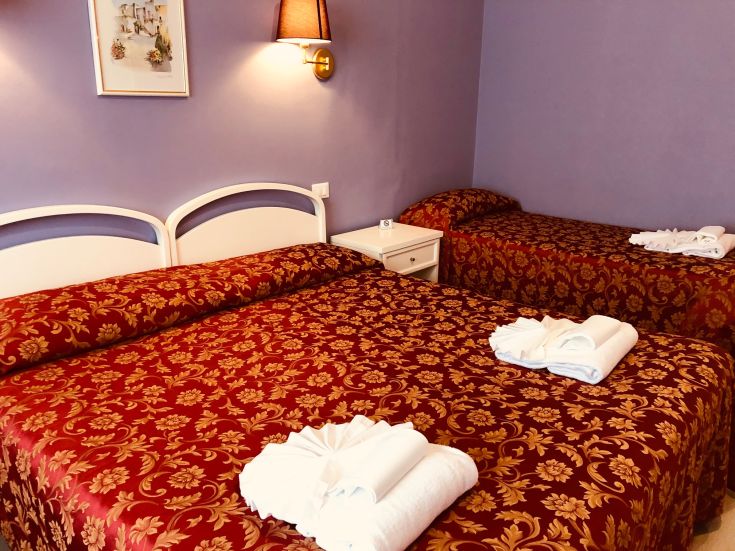 Chambre simple avec lits fleuris et mobilier essentiel. Espace idéal pour un séjour tranquille.