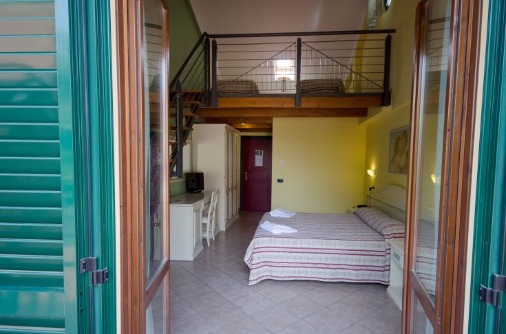 Intérieur d'une chambre avec mezzanine, caractérisé par des meubles simples et une lumière naturelle.
