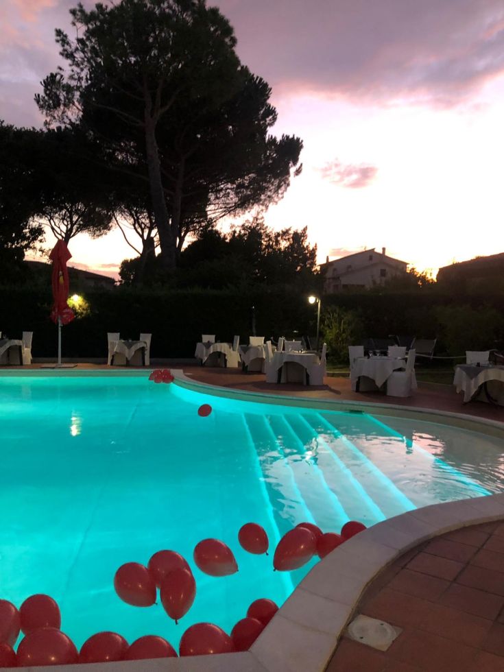 Une piscine bleue au crépuscule avec des ballons rouges flottants, créant une ambiance de soirée paisible.