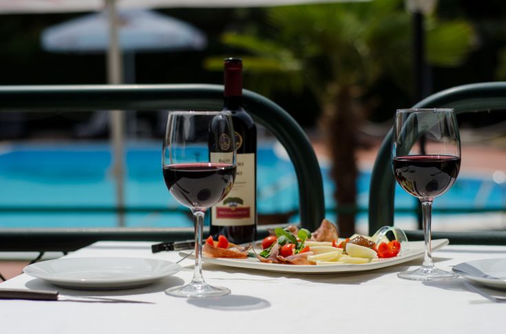 Déjeuner en plein air avec des plats frais et un verre de vin rouge, au bord de la piscine.