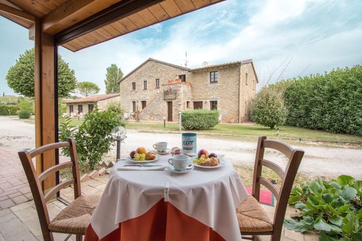 Breakfast served on a table with a view of a stone farmhouse surrounded by the countryside.