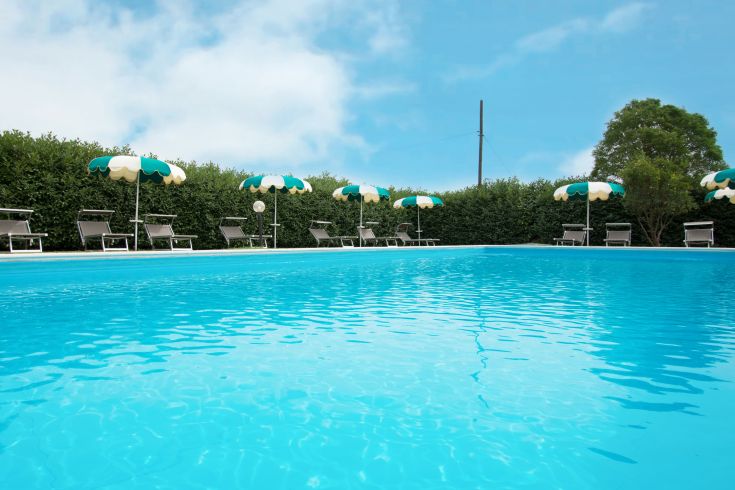 A blue swimming pool surrounded by green and white striped umbrellas, perfect for relaxing summer moments.