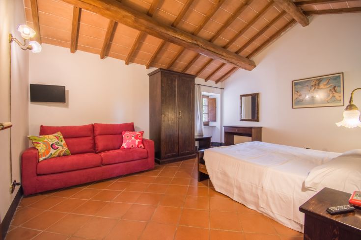 Cozy room with a red sofa, beds, and rustic elements, ideal for a peaceful stay.