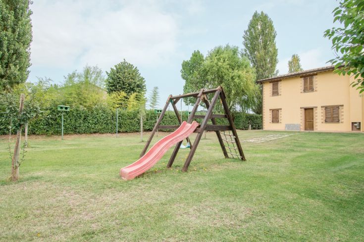 Outdoor play area featuring a red slide, surrounded by a well-kept green garden.