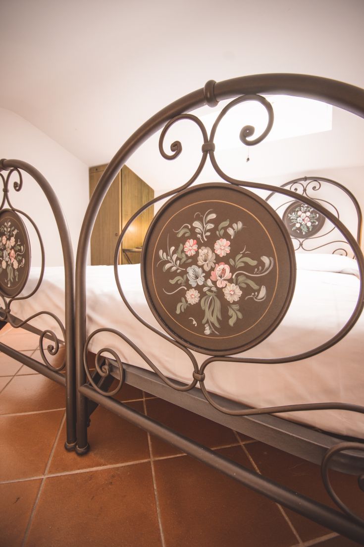 A cozy bedroom with a double bed featuring a wrought iron headboard. The space is bright.