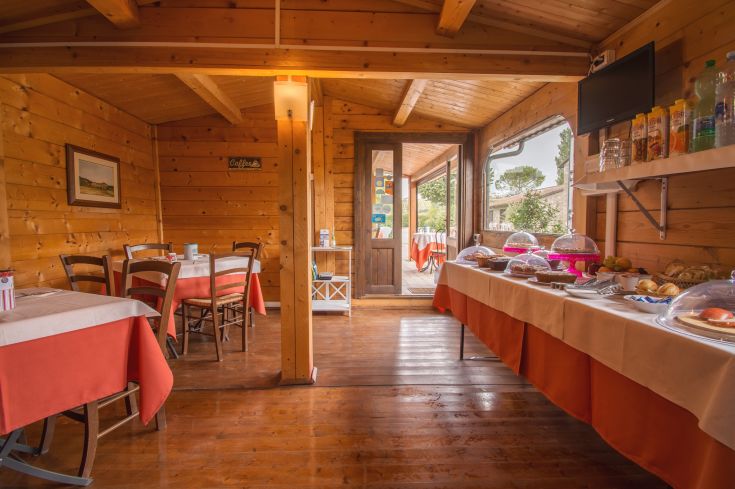 Simple wooden restaurant interior with tables and breakfast area, located in a tranquil setting.