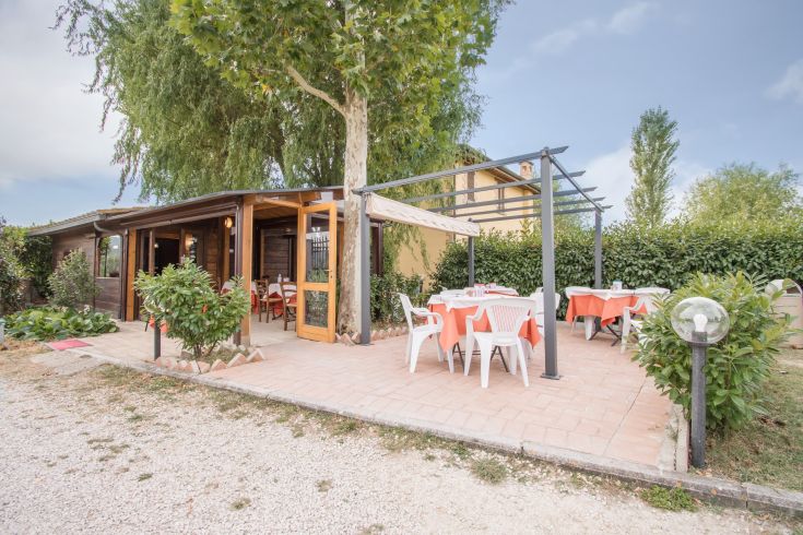 A rustic building with outdoor tables, surrounded by a calm green area.