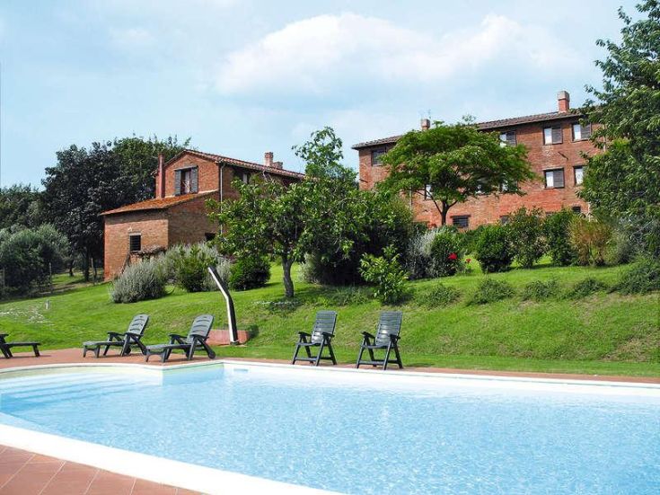 Der Pool ist von Grünflächen umgeben, mit Steinbelägen und alten Ziegelgebäuden in der Nähe.